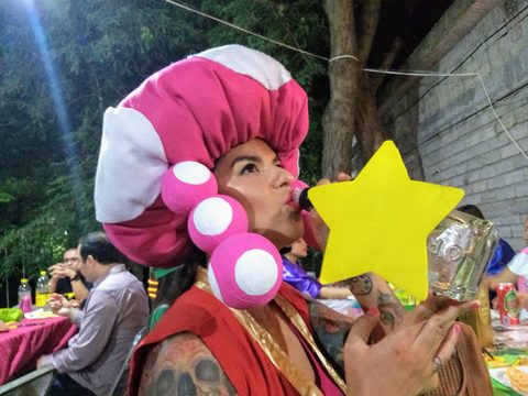 A person in a large pink and white costume headpiece blows a kiss through a star-shaped cutout. MJ, Colima, Mexico, February 9, 2019