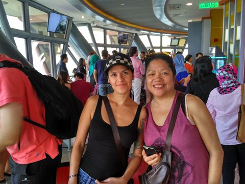 Two women smile for a photo in a crowded indoor terminal. MJ and Nadine, Kuala Lumpur, Malaysia, March 26, 2016