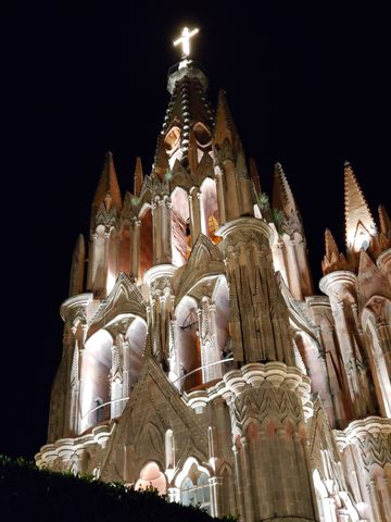 A large, ornate stone cathedral is illuminated against the dark night sky. La Sirena Gorda, San Miguel de Allende, Mexico, October 31, 2018