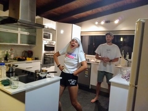 A woman in a nun costume poses playfully in a kitchen while a man watches in the background. James and Kate, Mooloolaba, Australia, December 10, 2017